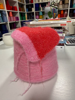Cone and knitted swatch of Essence 12000 fluffy alpaca blend yarn in pink and red.