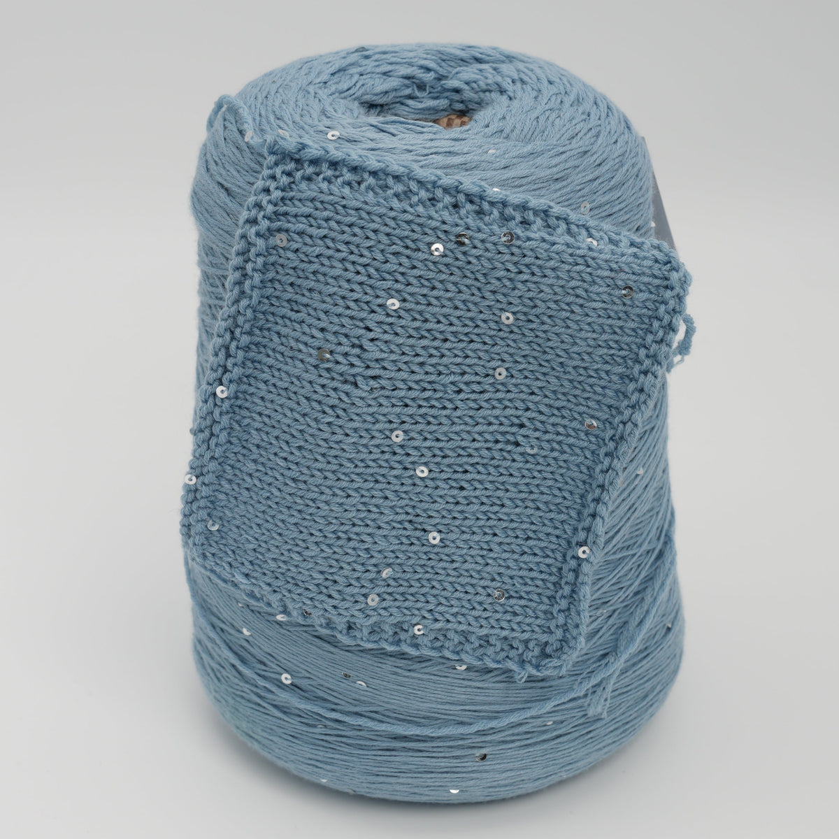 Cone and knitted swatch of Antilope 2/60 merino and sequin blend yarn in Stormy Sky.