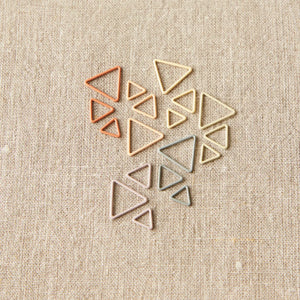 Mixed sizes of Cocoknits Earth Tone Triangle Stitch Markers grouped together on neutral fabric