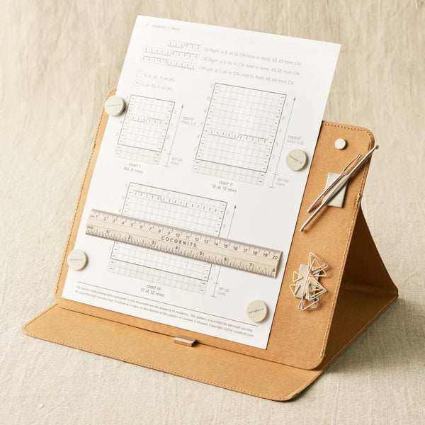 Cocoknits Maker's Board in Kraft holding a knitting pattern and tools