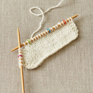 Cocoknits Small Round Stitch Markers shown on knitting needles with a light-colored work in progress