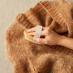 Cocoknits Sweater Care Brush. Hand using the wooden brush on a knitted sweater.