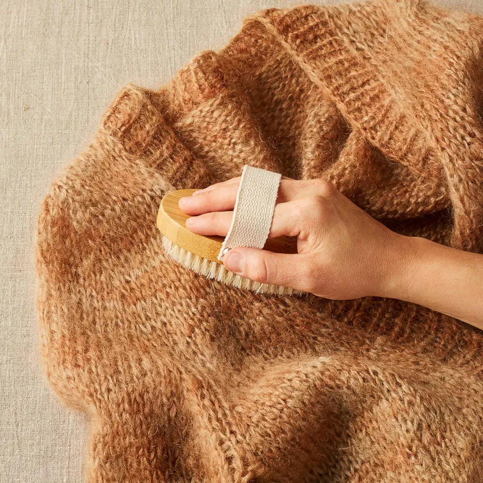 Cocoknits Sweater Care Brush. Hand using the wooden brush on a knitted sweater.