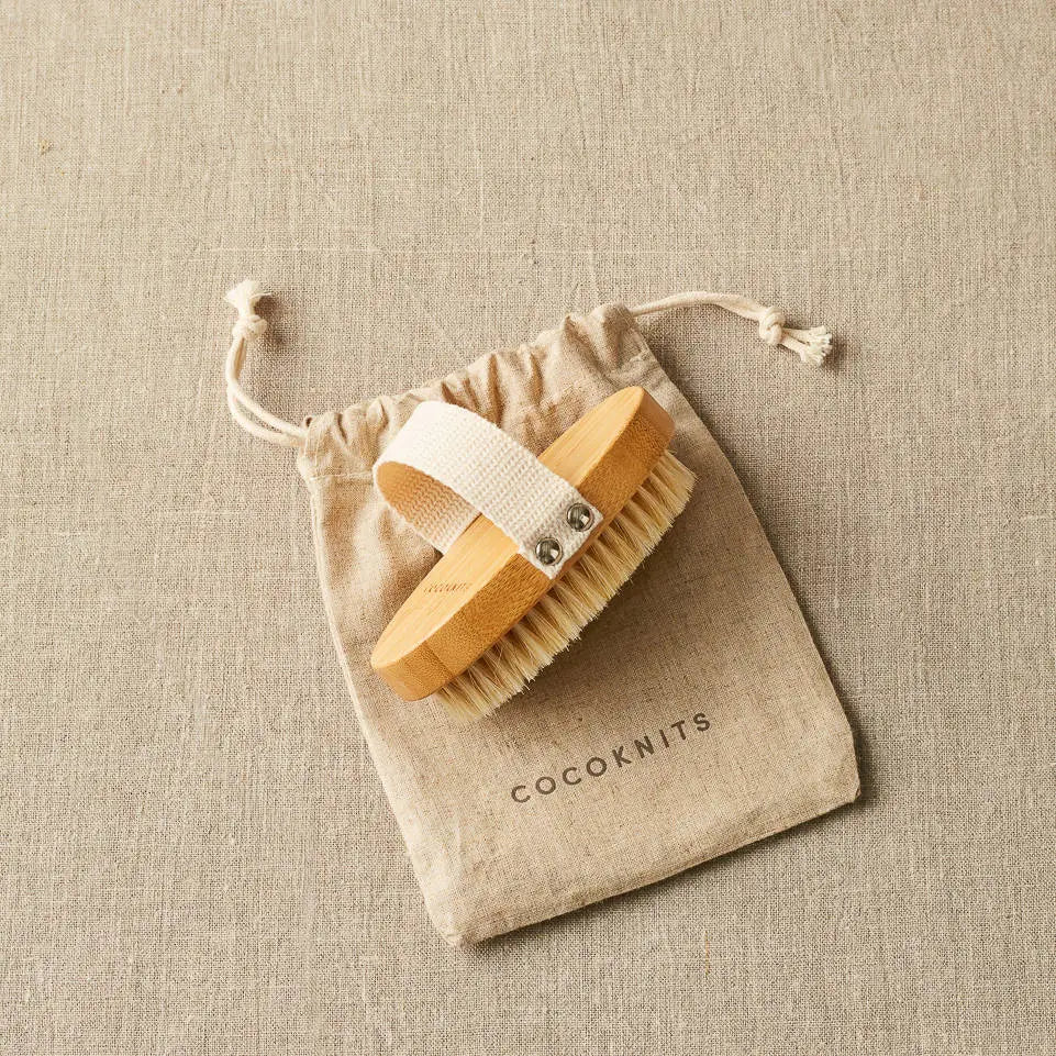 Cocoknits Sweater Care Brush. Wooden brush with its hand strap beside the drawstring bag.