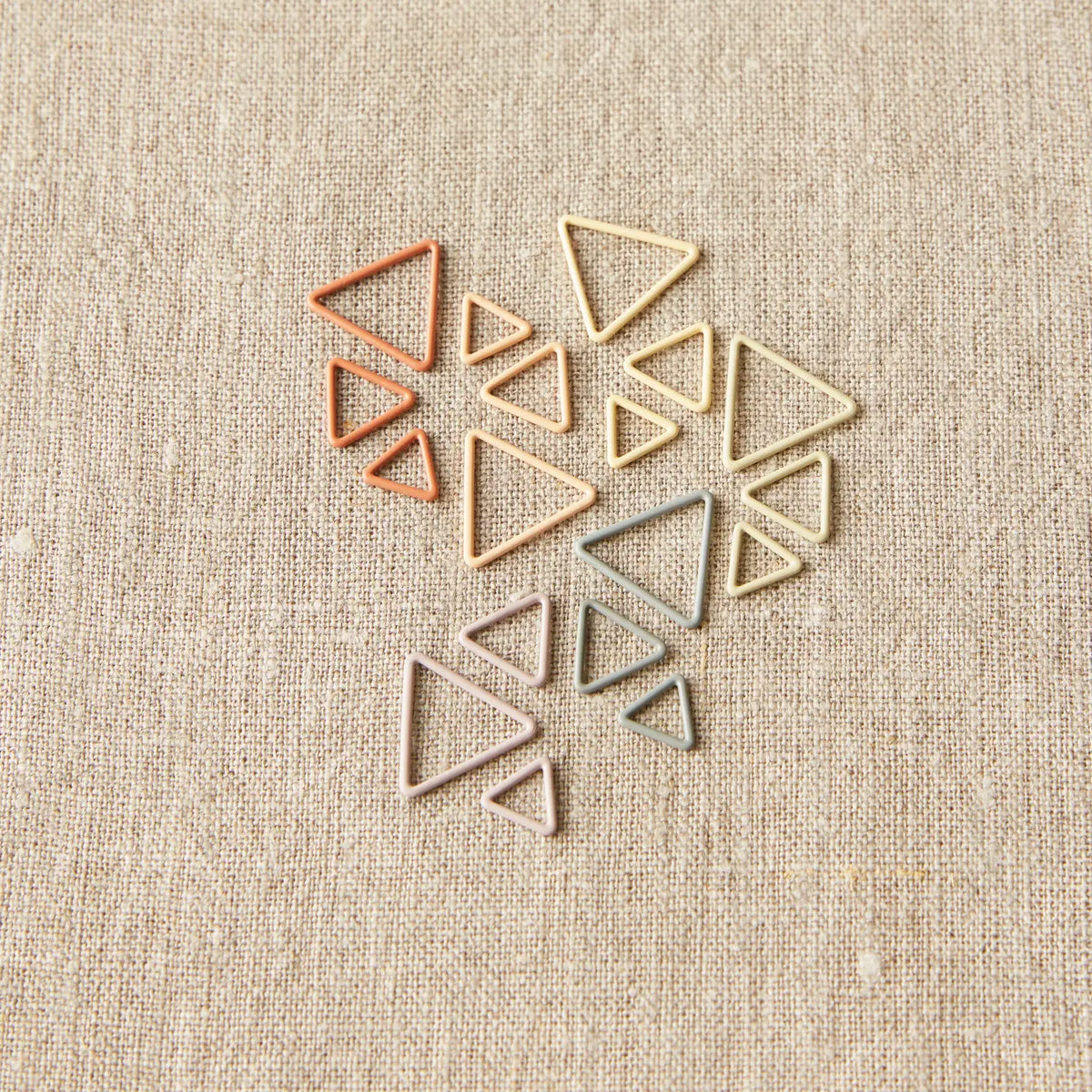Mixed sizes of Cocoknits Earth Tone Triangle Stitch Markers grouped together on neutral fabric