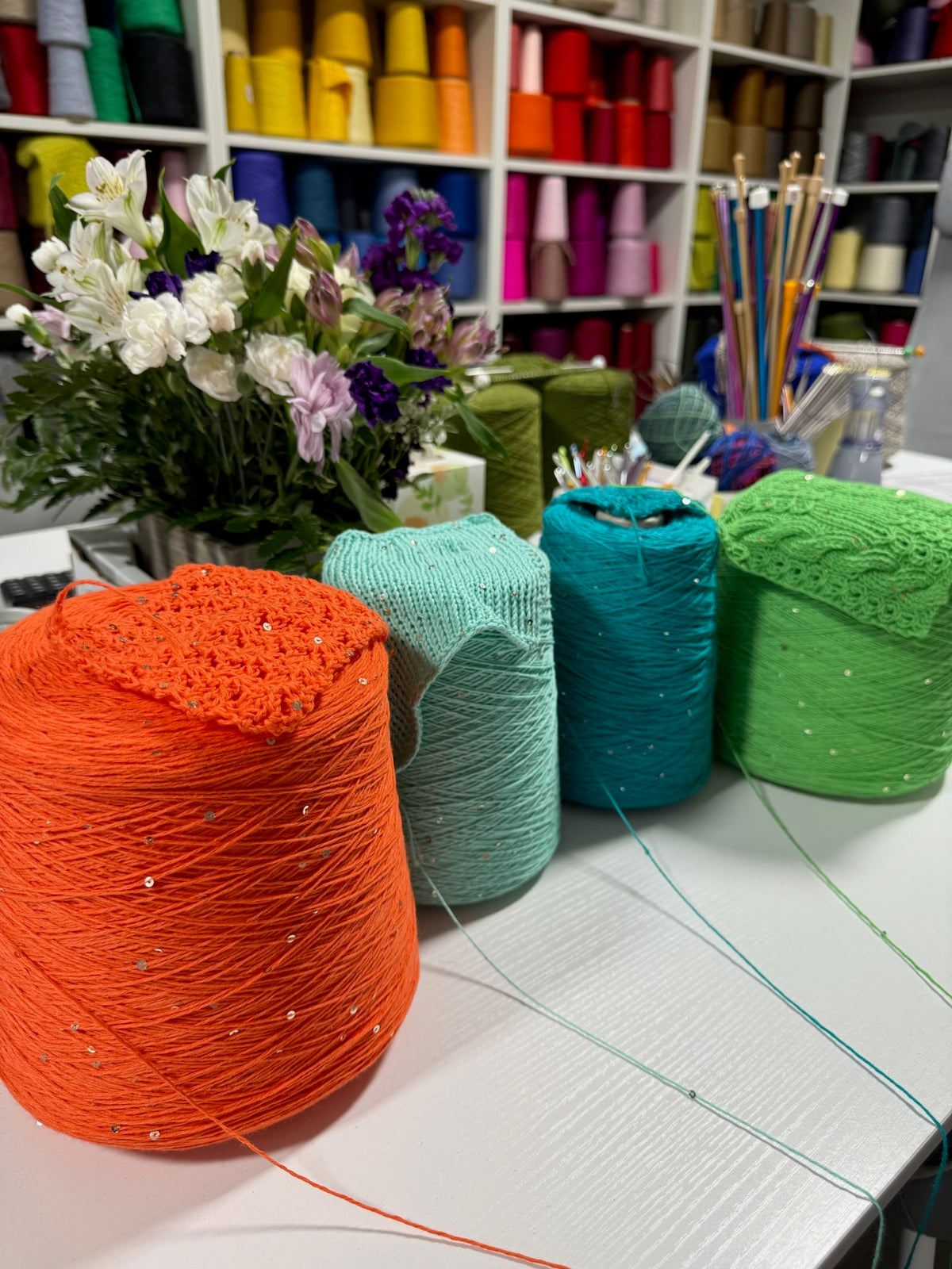 Cones and knitted swatches of Primavera NM4200 cotton and sequin blend yarn in Flame Orange, Mint Seafoam, Tropical Teal and Young Mint.