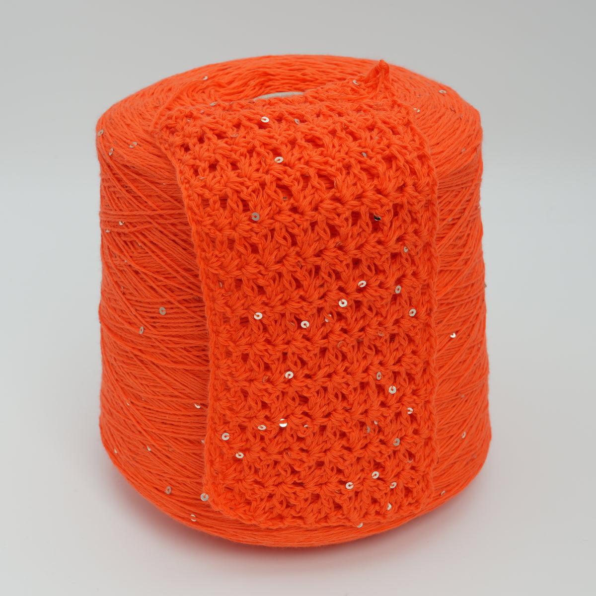Cone and knitted swatch of Primavera NM4200 cotton and sequin blend yarn in Flame Orange.