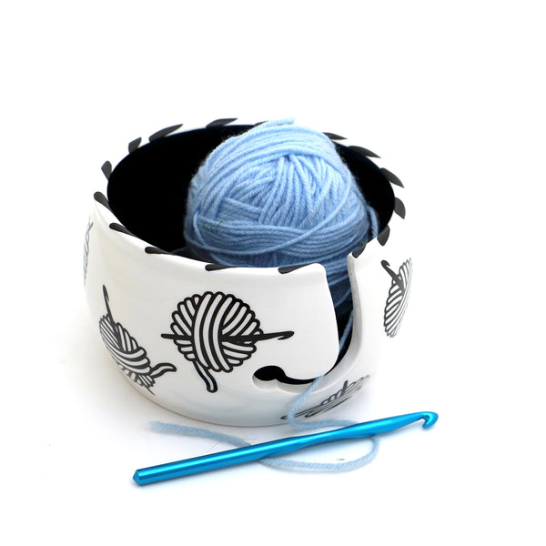 Yarn and Hooks Crochet Yarn Bowl. White bowl with a black interior, holding blue yarn beside a crochet hook.